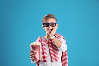 Photo of Cute boy in 3D glasses with popcorn bucket on color background