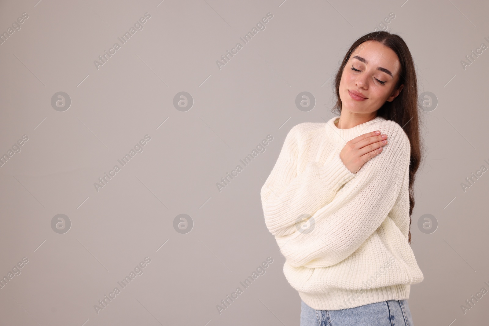 Photo of Beautiful young woman in stylish warm sweater on grey background, space for text