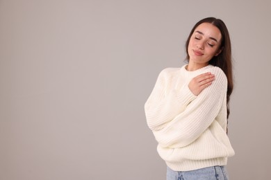 Photo of Beautiful young woman in stylish warm sweater on grey background, space for text