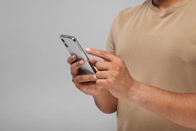 Photo of Man sending message via smartphone on grey background, closeup. Space for text