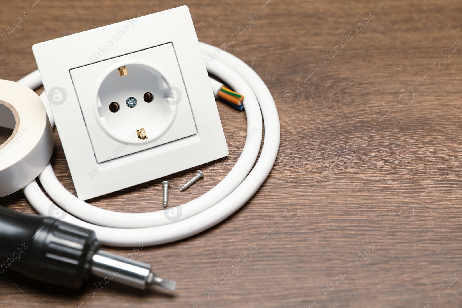 Photo of Power socket, screwdriver, cable and insulating tape on wooden table. Space for text