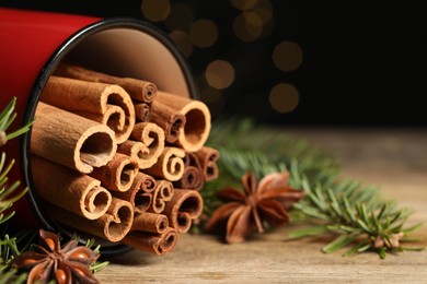 Many cinnamon sticks, anise stars and fir branches on wooden table, closeup. Space for text