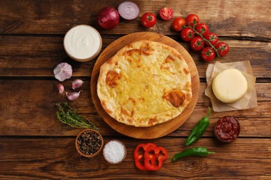 Photo of Delicious khachapuri with cheese, sauces, vegetables and spices on wooden table, flat lay