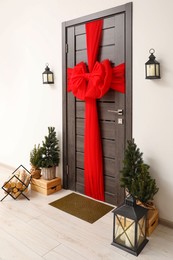 Photo of Wooden door with beautiful red bow near evergreen trees ,logs and lanterns. Christmas decoration