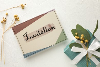 Photo of Beautiful card with word Invitation, eucalyptus leaves and gift box on white table, flat lay