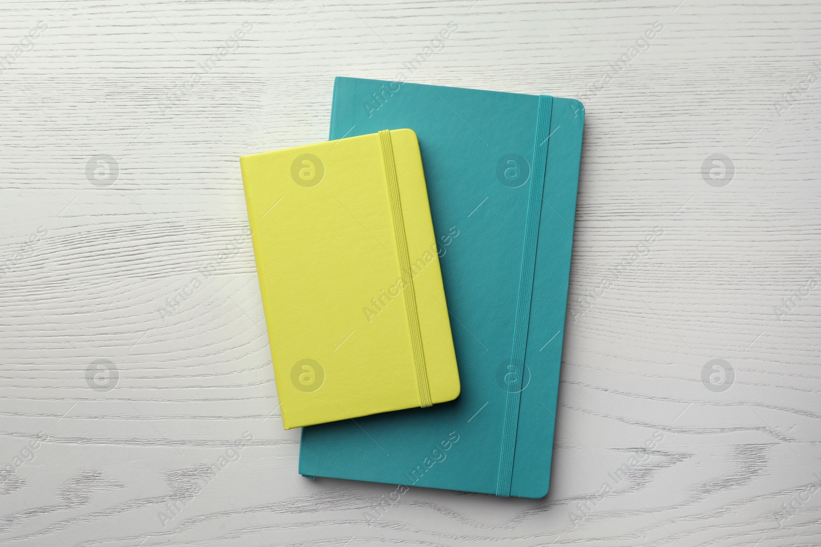 Photo of Yellow and turquoise planners on white wooden table, top view