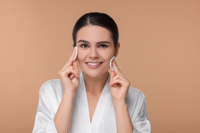Young woman cleaning her face with cotton pads on beige background