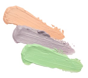 Strokes of pink, green and purple color correcting concealers isolated on white, top view