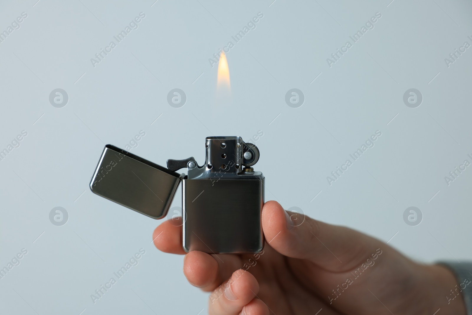 Photo of Man holding lighter with burning flame against light grey background, closeup