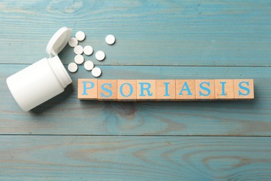Photo of Word Psoriasis made of cubes with letters and pills on light blue wooden table, flat lay