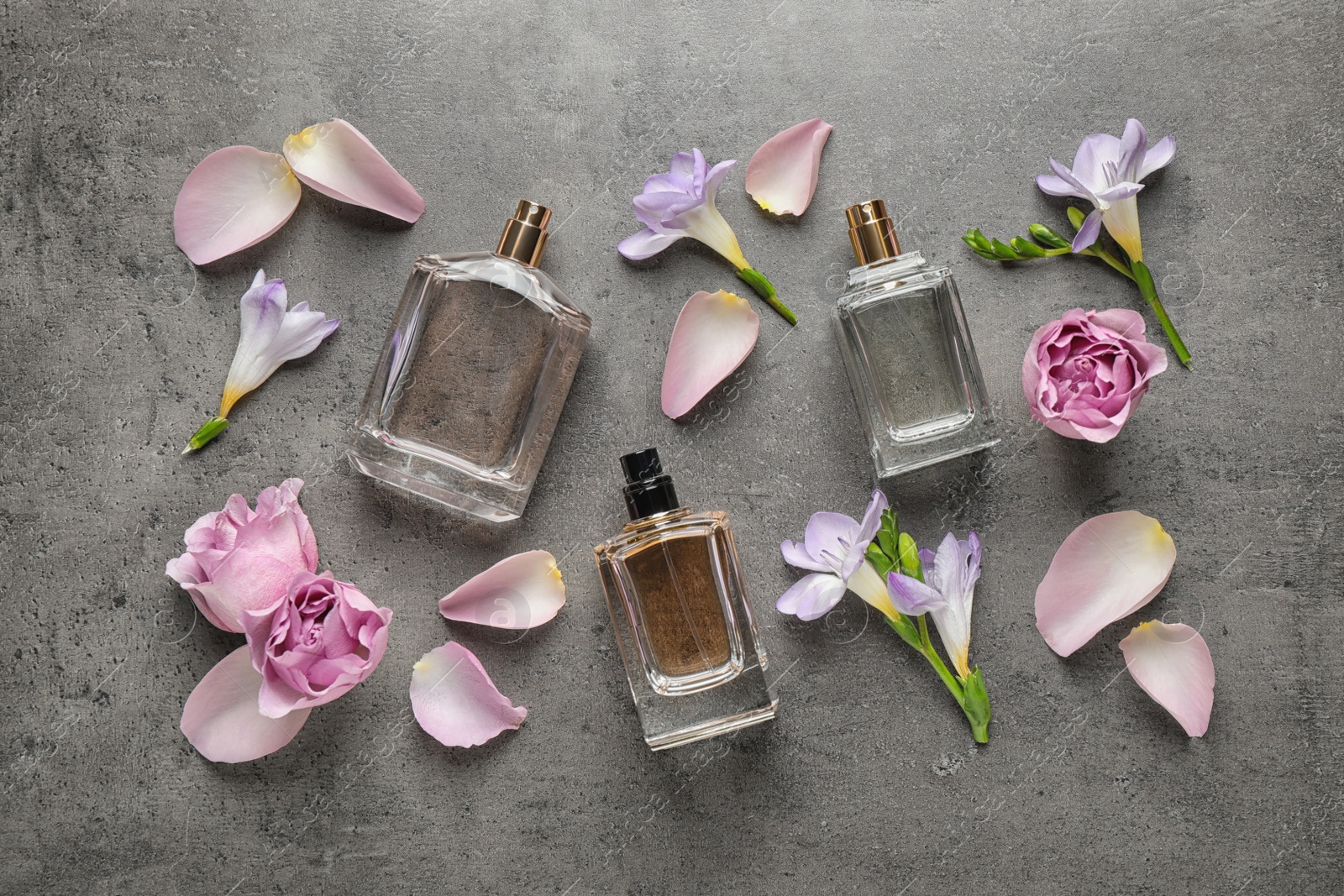 Photo of Flat lay composition of different perfume bottles, roses and freesia flowers on dark textured background