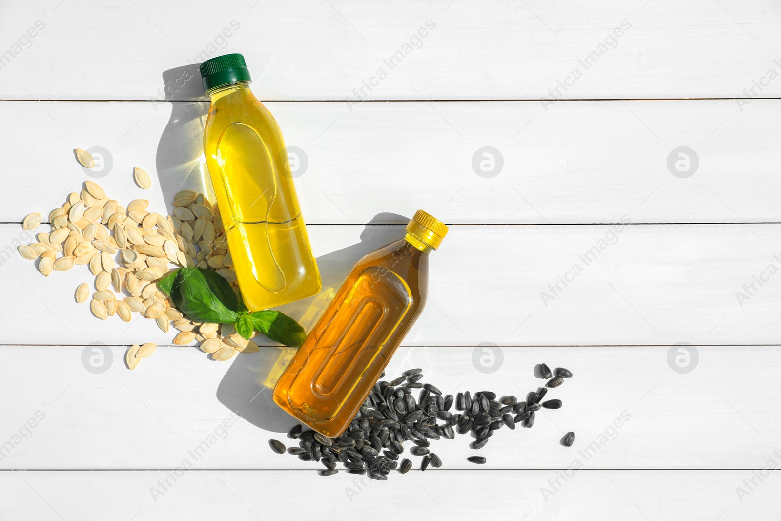 Photo of Different cooking oils and seeds on white wooden table, flat lay. Space for text