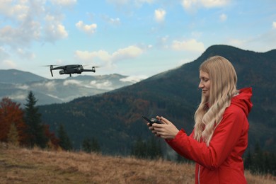 Young woman operating modern drone with remote control in mountains