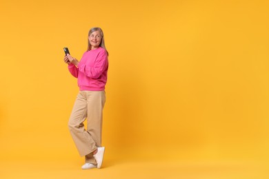 Senior woman with phone on orange background, space for text