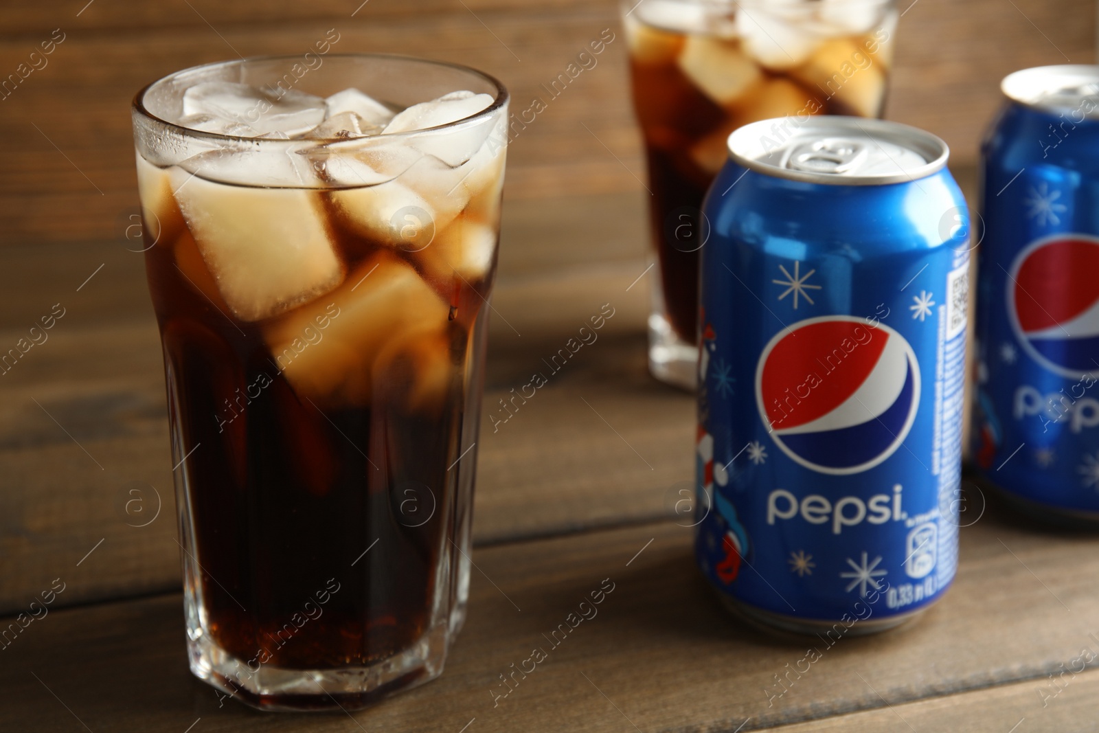Photo of MYKOLAIV, UKRAINE - FEBRUARY 10, 2021: Glasses and cans of Pepsi on wooden table