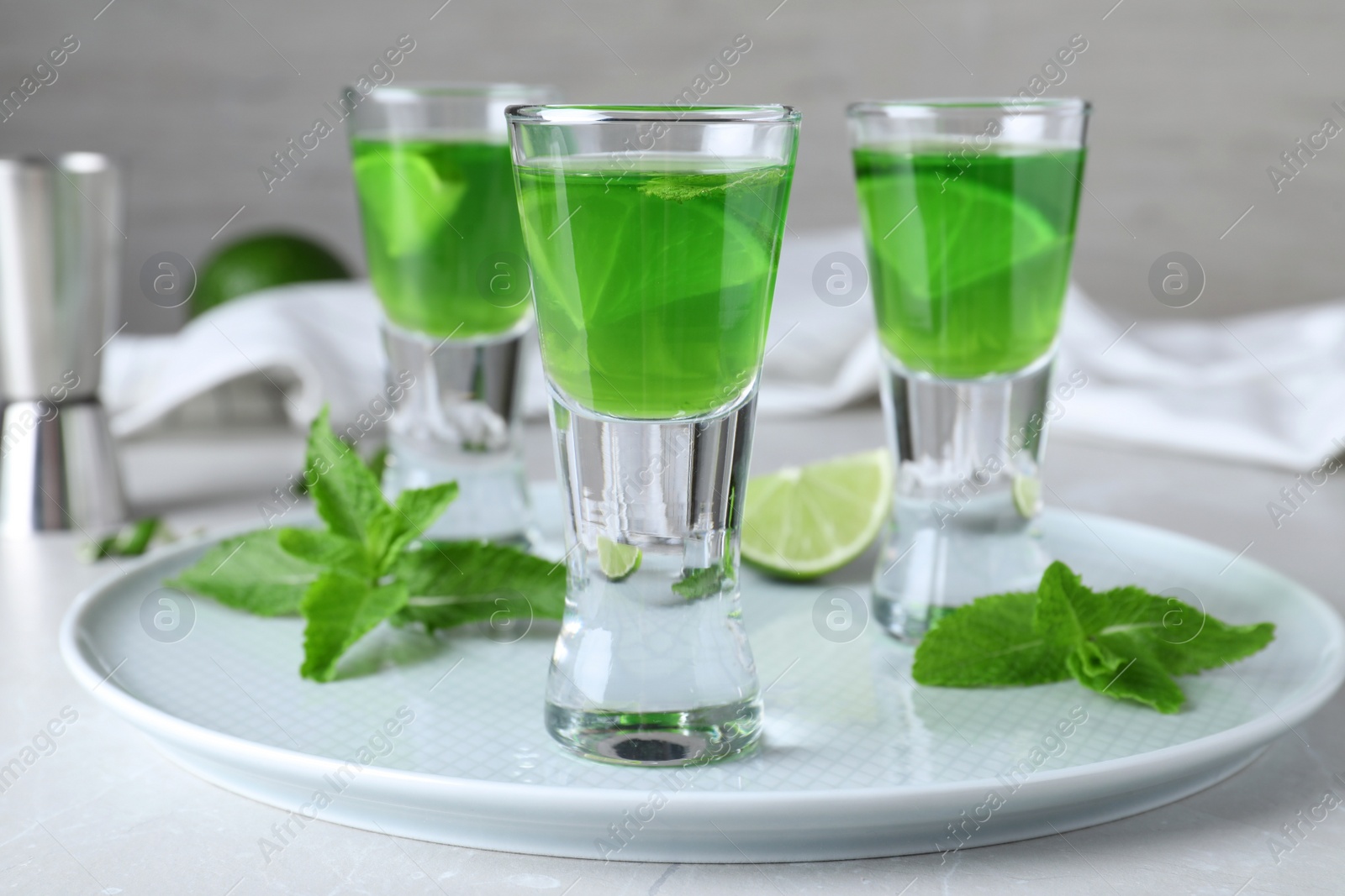 Photo of Delicious mint liqueur with lime and green leaves on white table, closeup