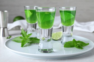 Delicious mint liqueur with lime and green leaves on white table, closeup