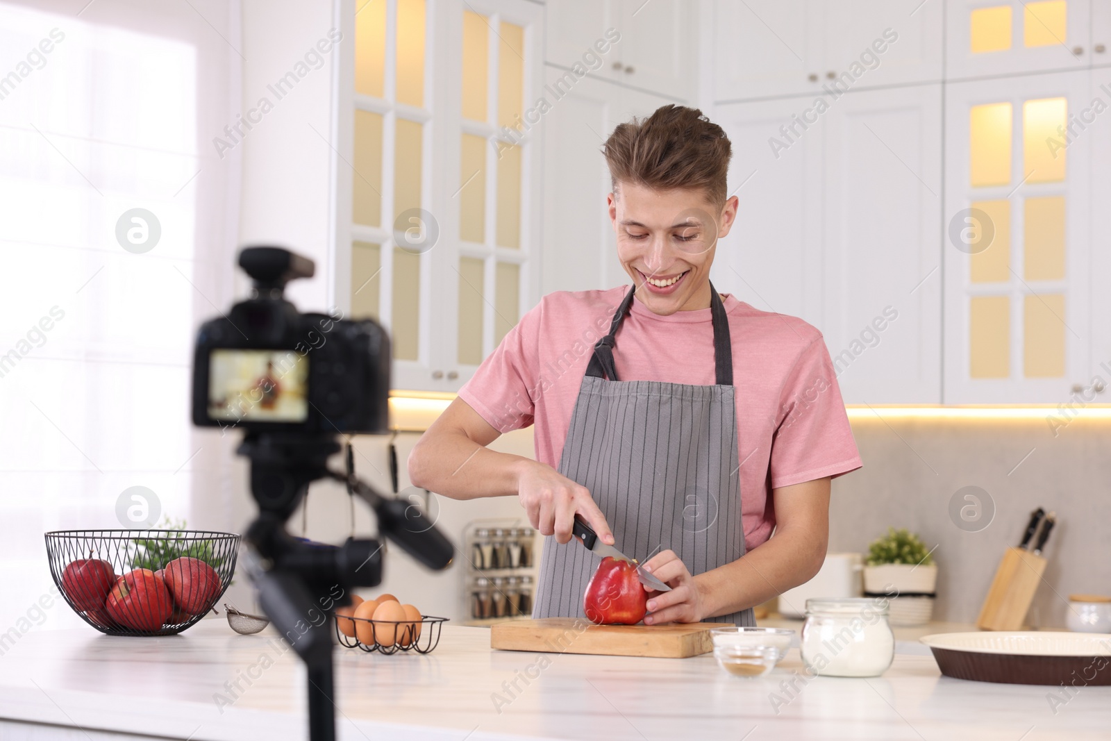 Photo of Smiling food blogger cooking while recording video in kitchen