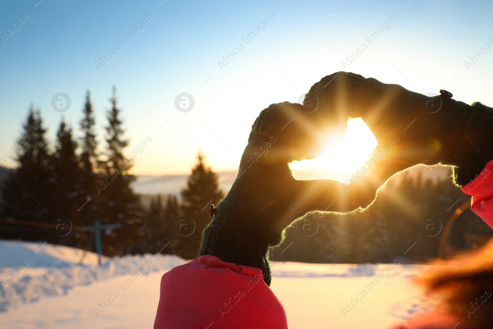 Photo of Woman making heart with hands outdoors at sunset, closeup. Winter vacation