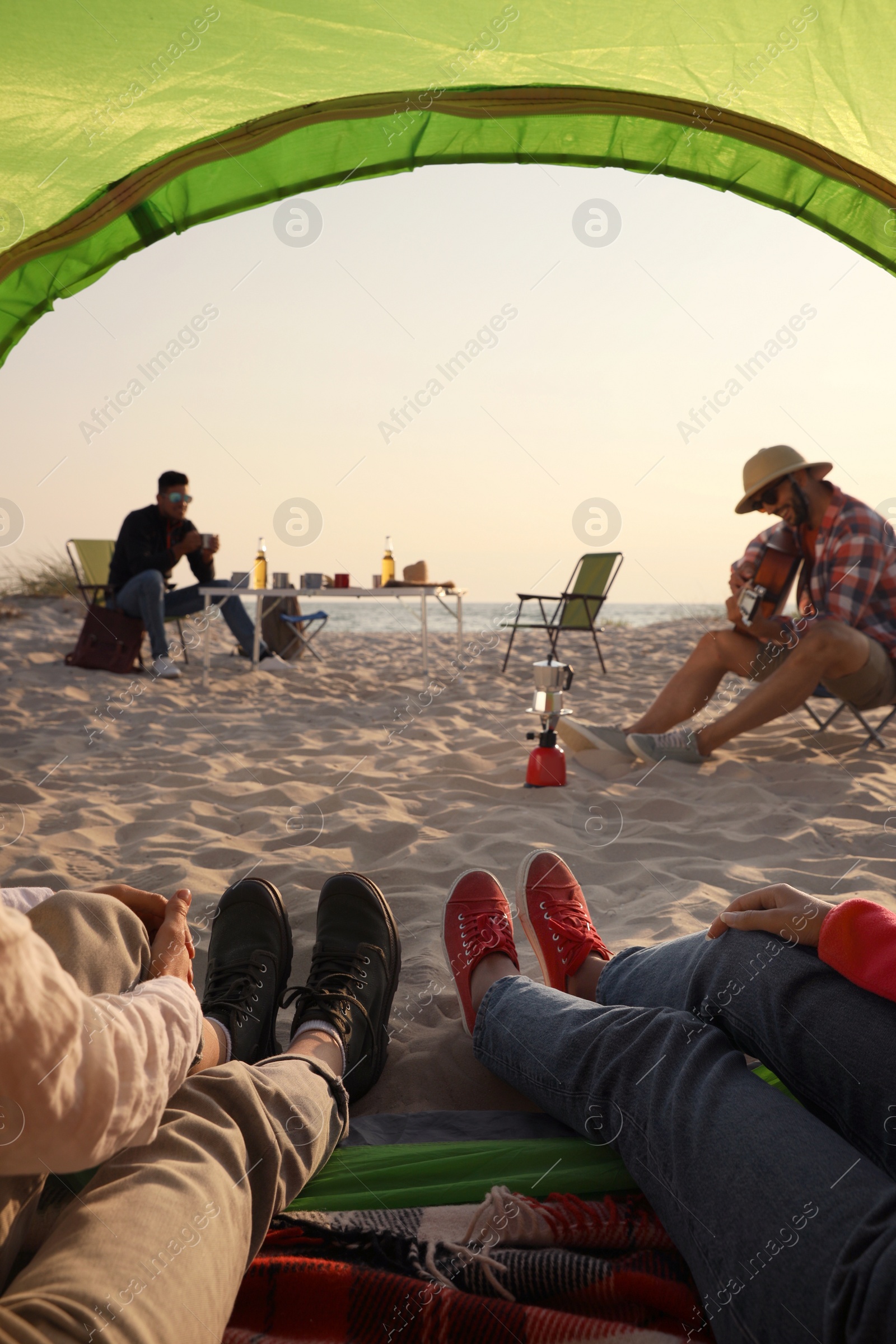 Photo of Friends resting on sandy beach, closeup. View from camping tent