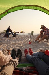 Photo of Friends resting on sandy beach, closeup. View from camping tent