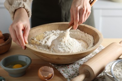 Woman kneading dough with spoon in bowl at wooden table indoors, closeup