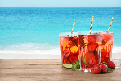 Tasty refreshing drink on wooden table against sea