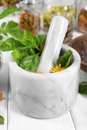 Photo of Mortar with pestle and many different medicinal herbs on white wooden table, closeup