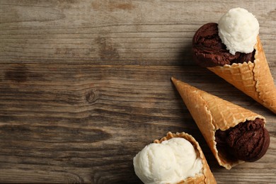 Photo of Ice cream scoops in wafer cones on wooden table, flat lay. Space for text