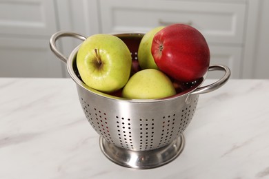 Photo of Fresh apples in colander on white marble table indoors