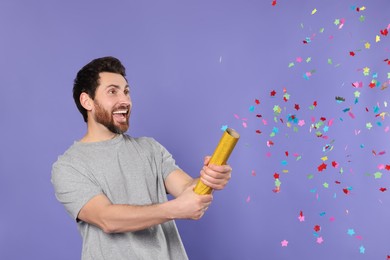 Photo of Emotional man blowing up party popper on violet background