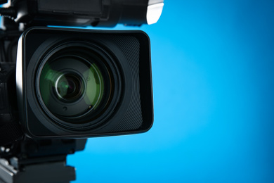 Professional video camera on blue background, closeup. Space for text