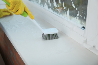 Photo of Woman cleaning window sill with brush, closeup