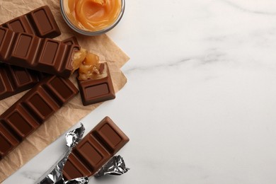 Photo of Tasty chocolate bars and bowl of caramel on white table, flat lay. Space for text