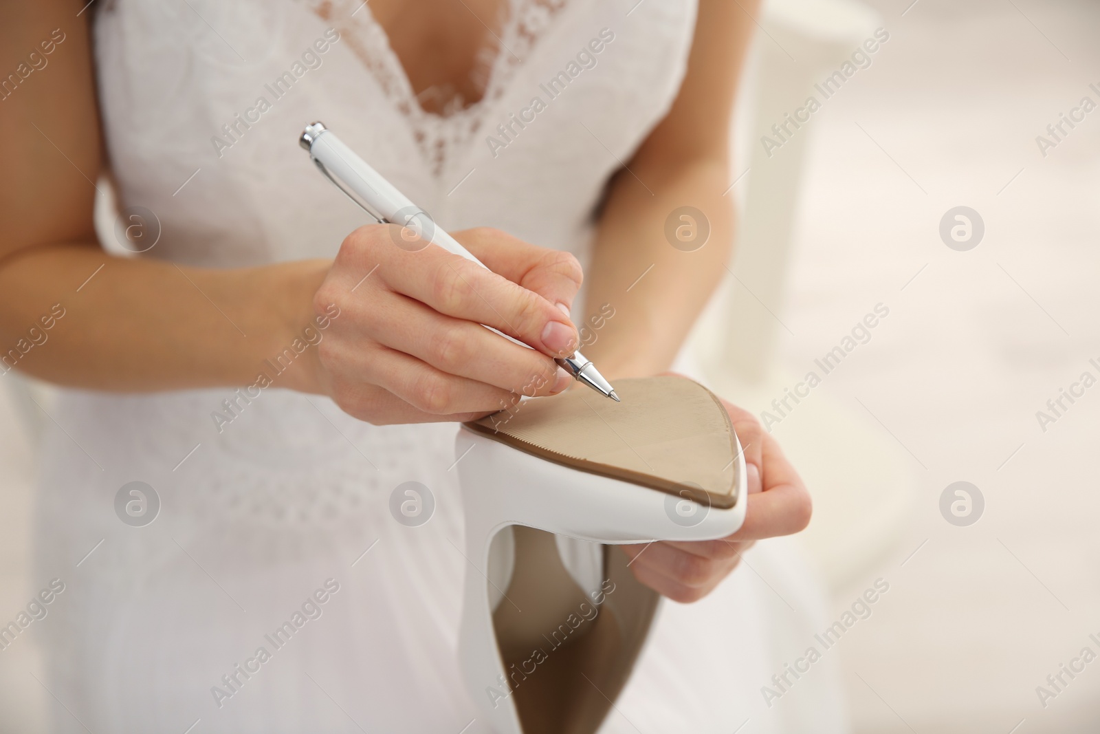 Photo of Young bride writing on her shoe indoors, closeup. Wedding superstition