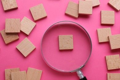 Magnifying glass and pieces of wood on pink background, flat lay