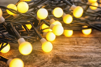 Photo of Glowing Christmas lights on wooden table, closeup