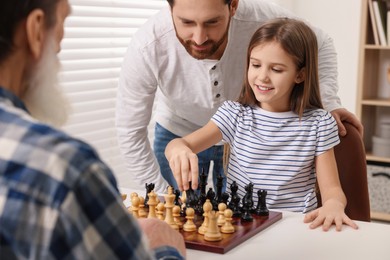 Family playing chess together at table in room