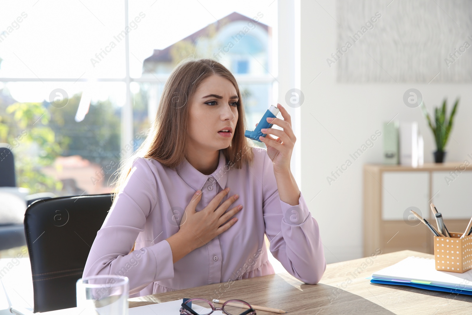 Photo of Young woman with asthma inhaler at table in light room