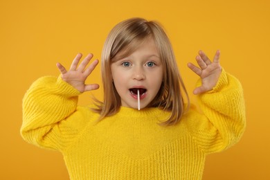 Photo of Emotional girl with lollipop on orange background