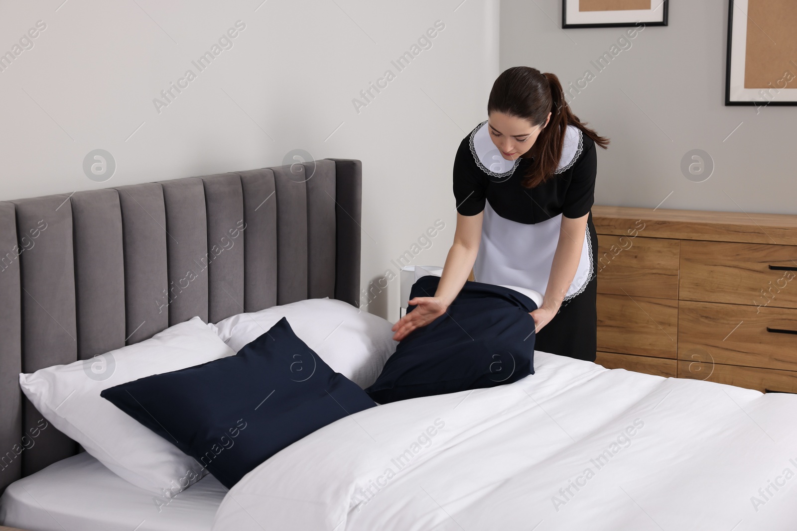 Photo of Young chambermaid making bed in hotel room