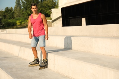Handsome young man roller skating outdoors, space for text