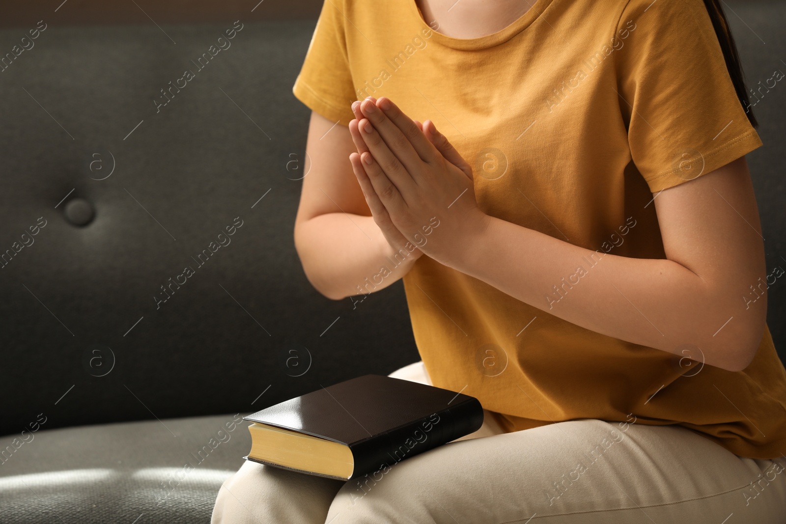 Photo of Religious woman praying over Bible indoors, closeup