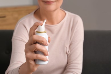 Photo of Woman holding nasal spray indoors, focus on bottle