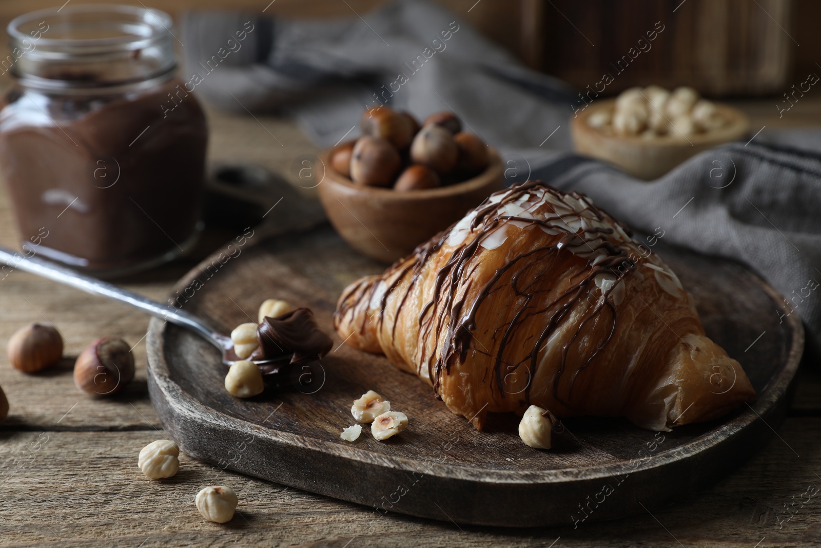 Photo of Delicious croissant with chocolate and nuts on wooden table