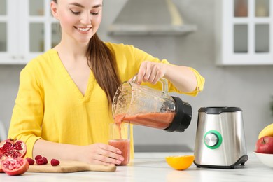 Photo of Woman pouring tasty smoothie into glass at white table in kitchen