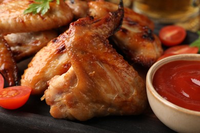 Delicious baked chicken wings and sauce on dark grey table, closeup