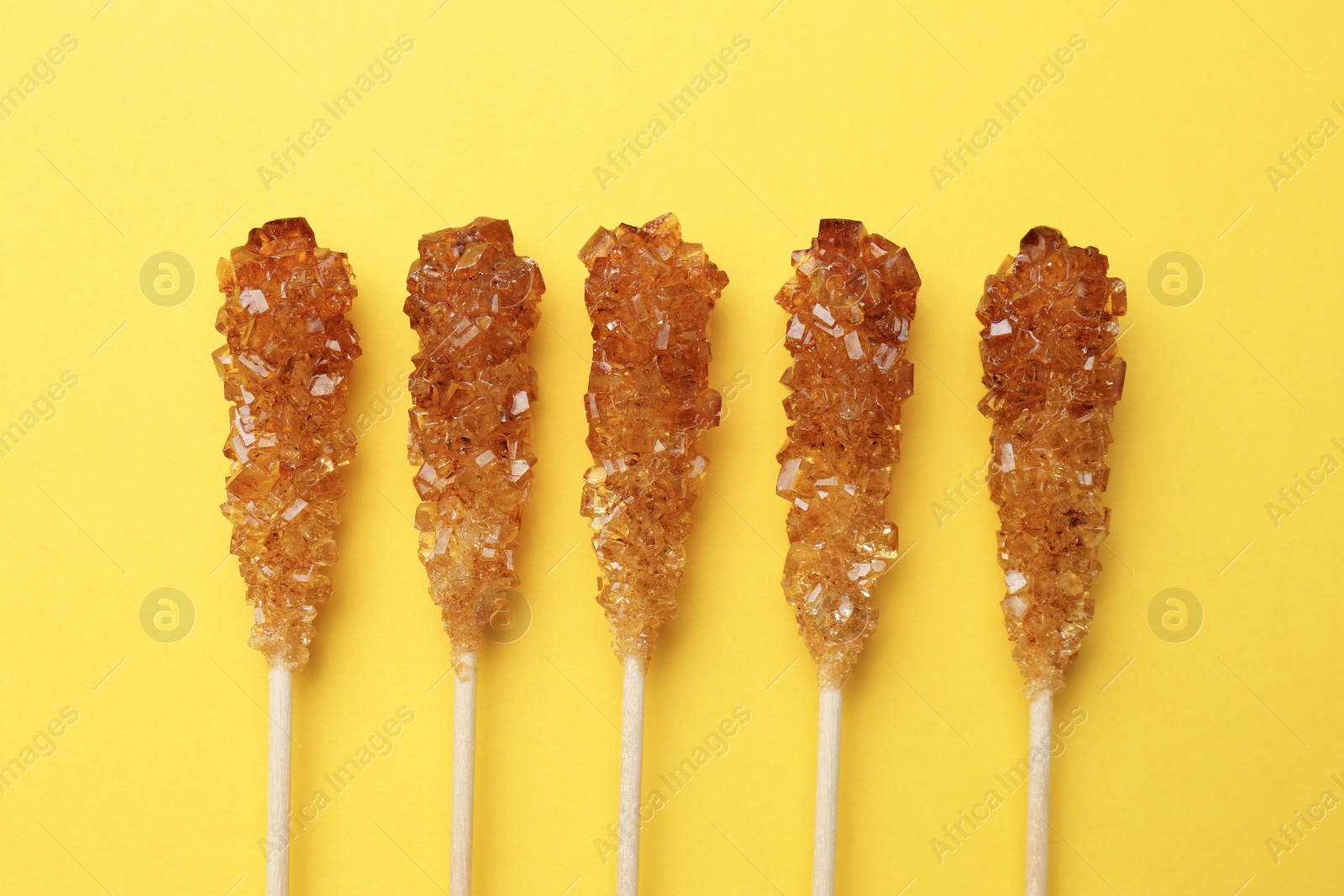 Photo of Wooden sticks with sugar crystals on yellow background, flat lay. Tasty rock candies