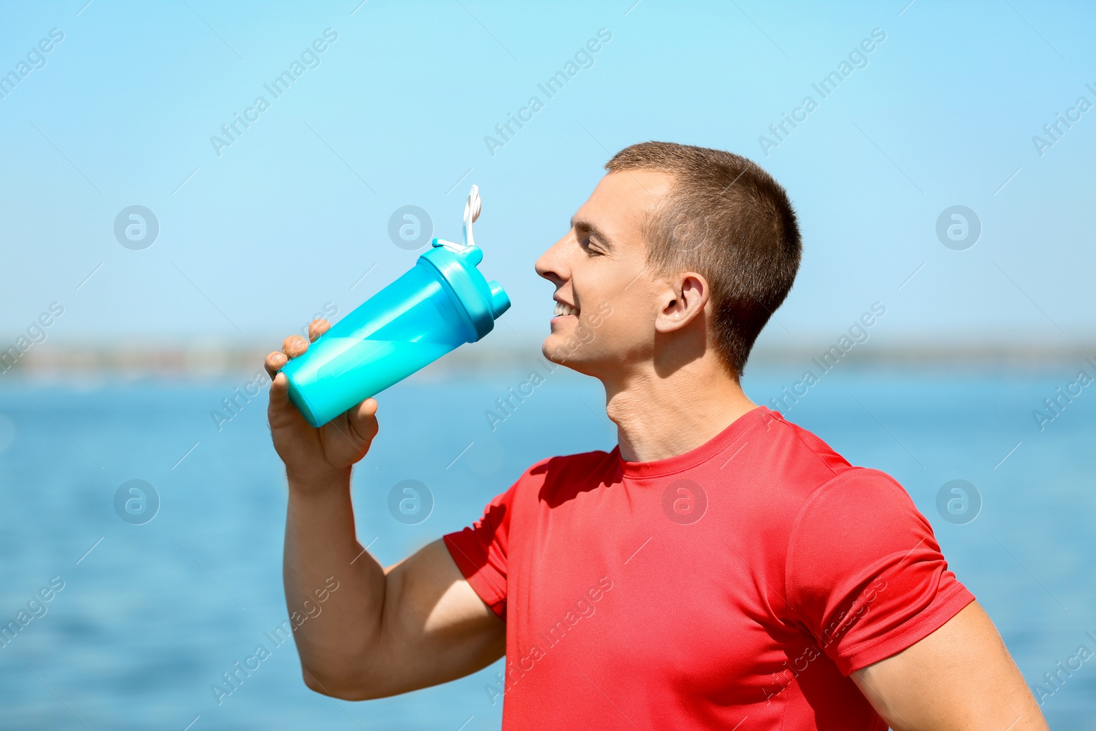 Photo of Athletic young man drinking protein shake at riverside