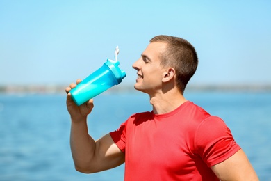 Photo of Athletic young man drinking protein shake at riverside